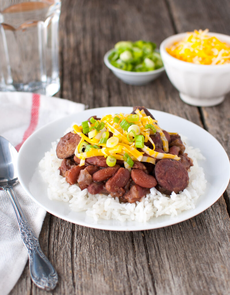 Plate of red beans and rice next to bowl of grated cheese and bowl of green onions.