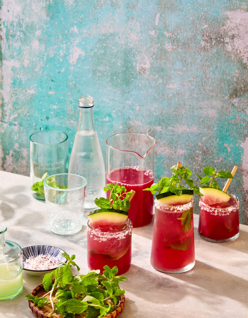Several glasses of watermelon mocktails with fresh mint, lime juice, and bottle of sparkling water.