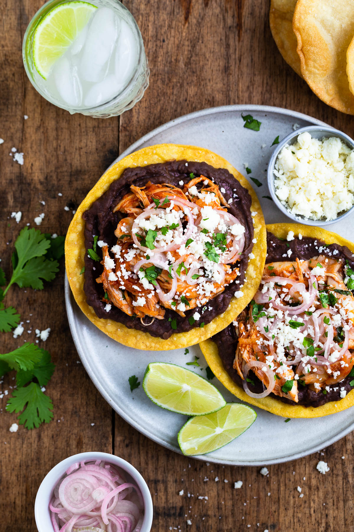 Some chicken tinga tostadas on a gray plate with pickled shallots and extra cheese on the side.
