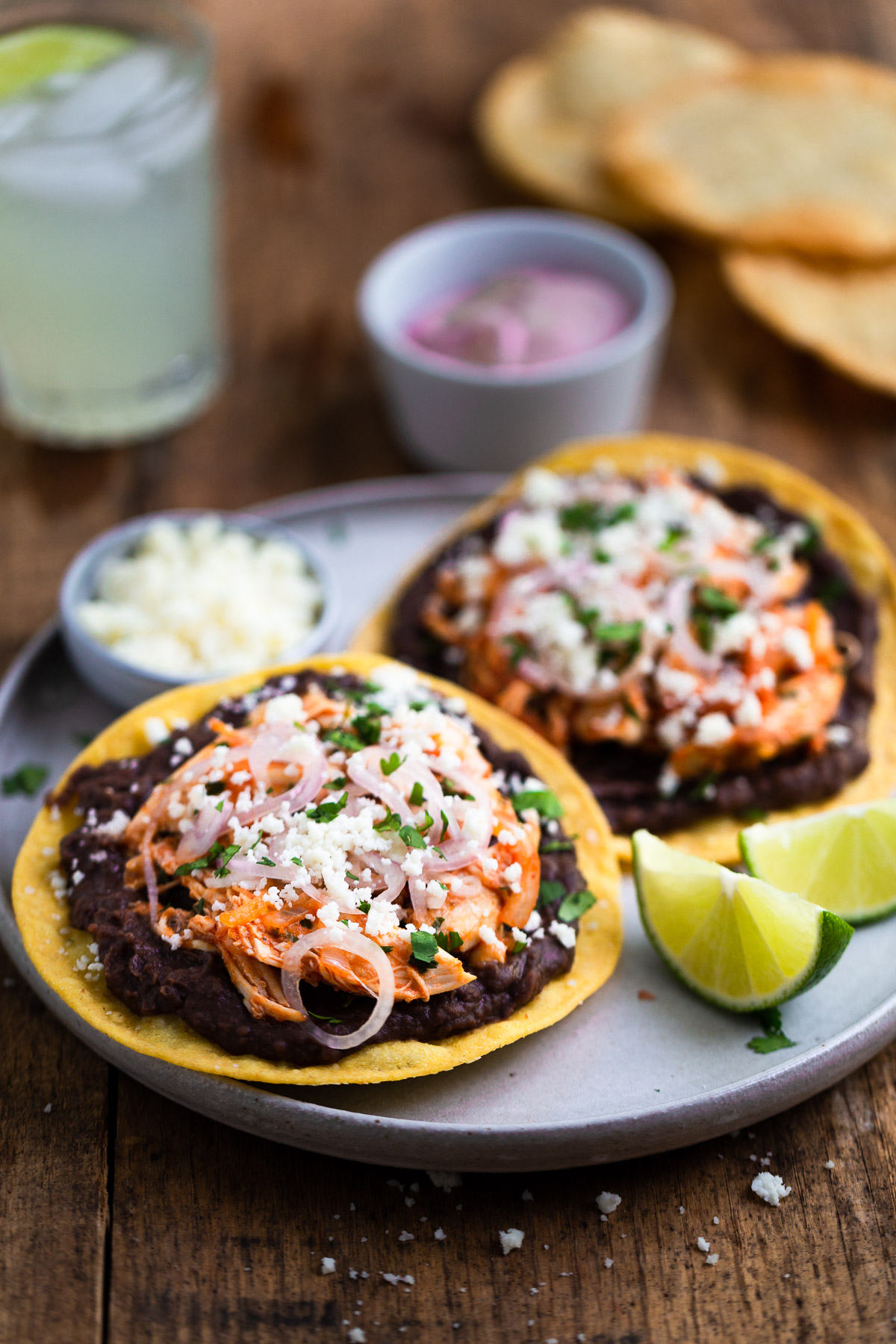 Tostadas topped with refried beans, shredded chicken, pickled shallots, and cotija cheese.
