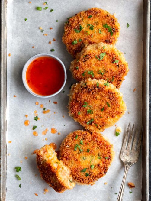 Salmon cakes on parchment paper with a small bowl of sweet chili sauce on the side.