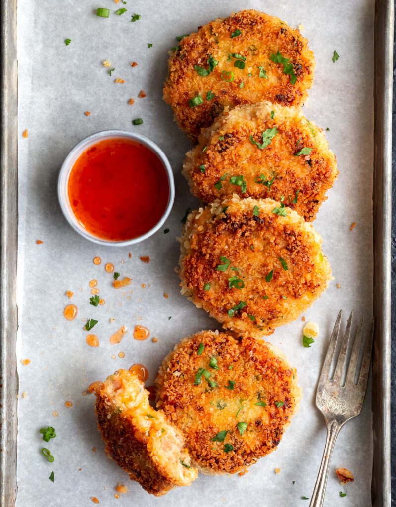 Salmon cakes on parchment paper with a small bowl of sweet chili sauce on the side.