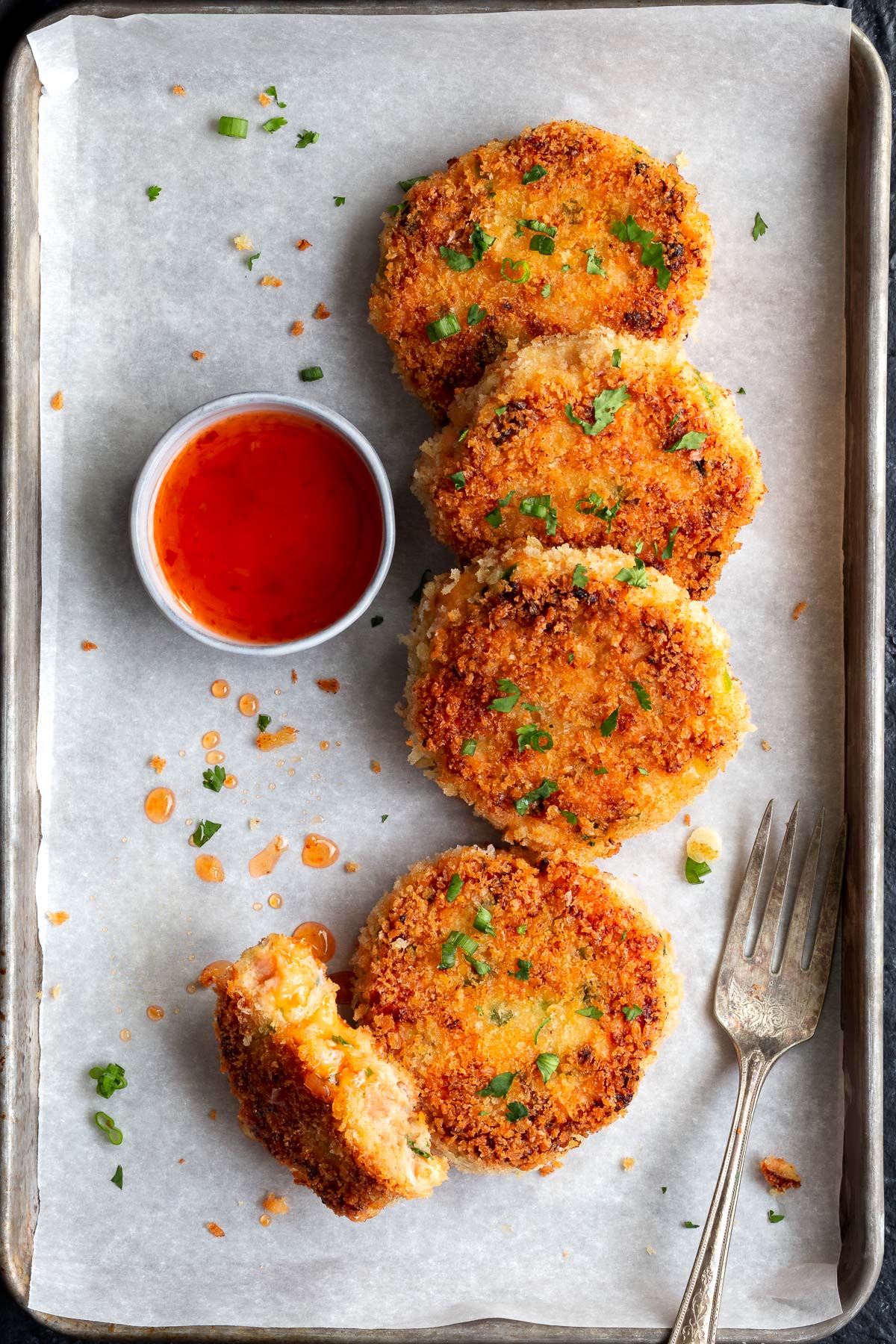Salmon cakes on parchment paper with a small bowl of sweet chili sauce on the side.