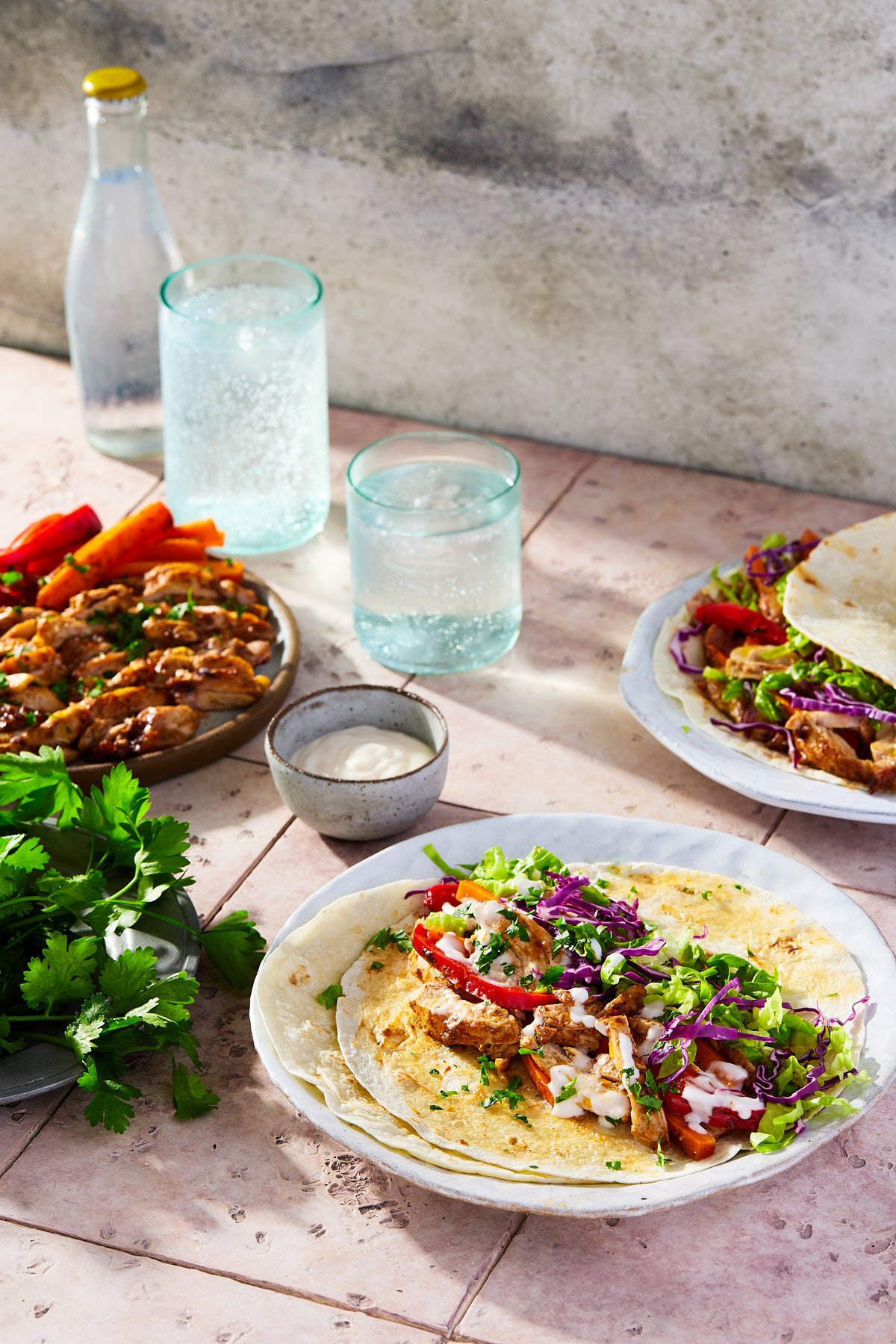 Two plates of chicken shawarma next to a plate of herbs.