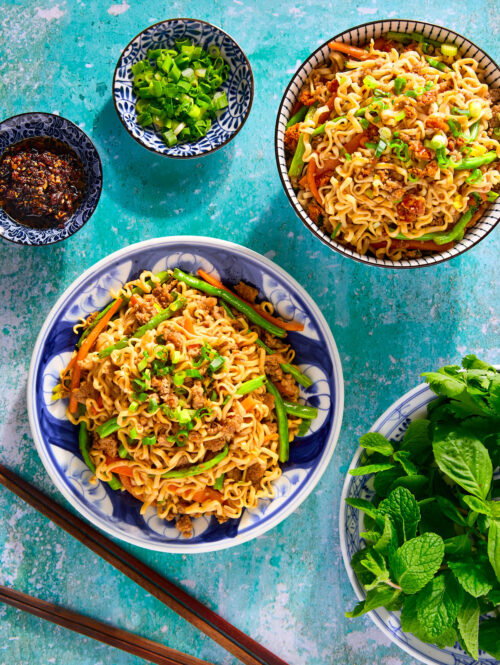 Stir-fried noodles on a plate with herbs and chili crisp on the side.