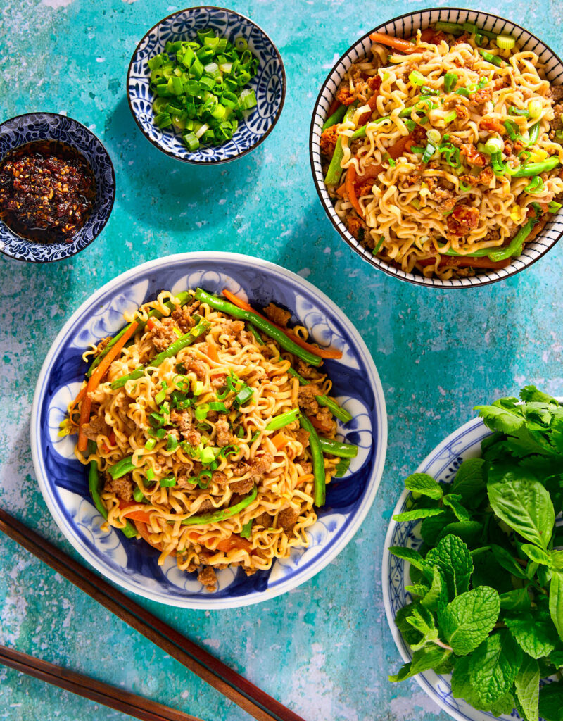 Stir-fried noodles on a plate with herbs and chili crisp on the side.