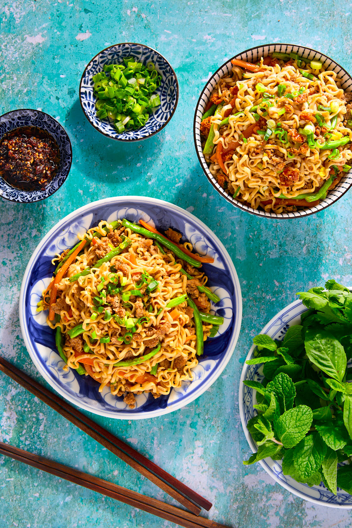 Stir-fried noodles on a plate with herbs and chili crisp on the side.