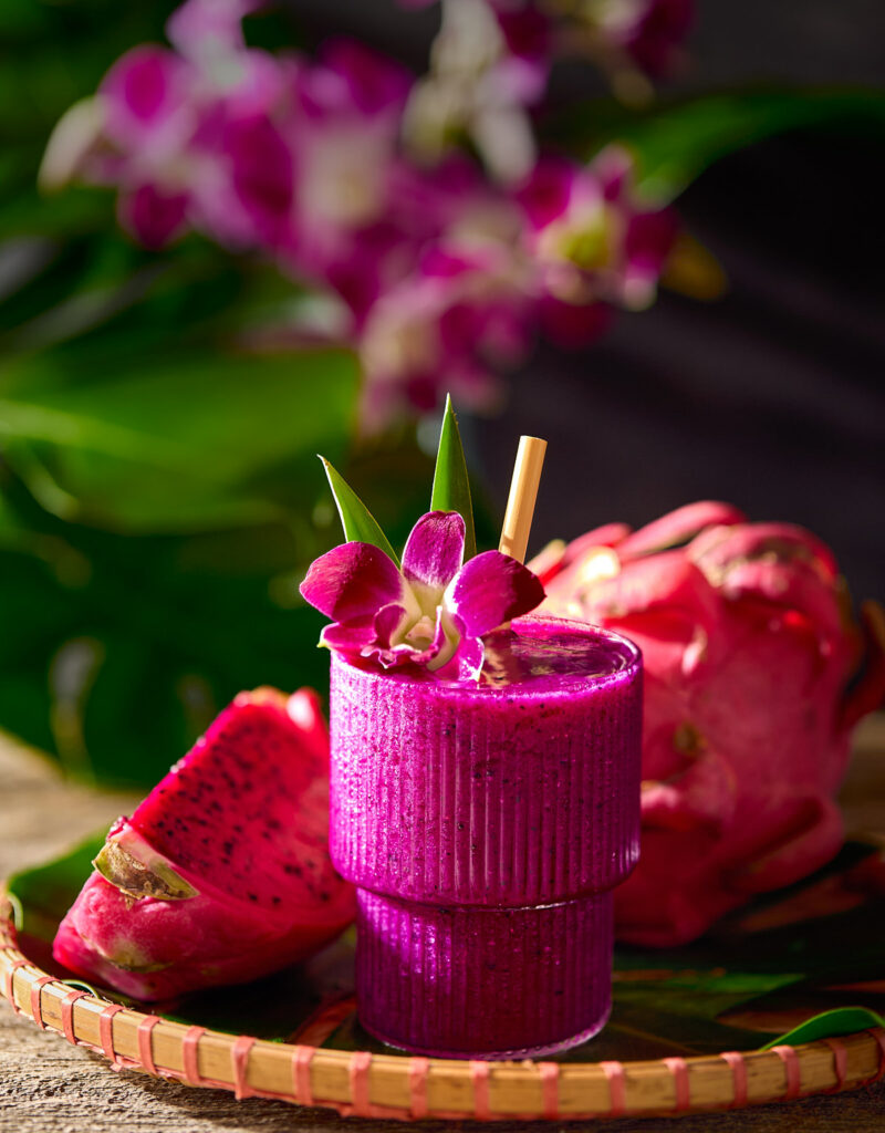 Glass of dragonfruit mocktail next to a cut piece of dragonfruit.