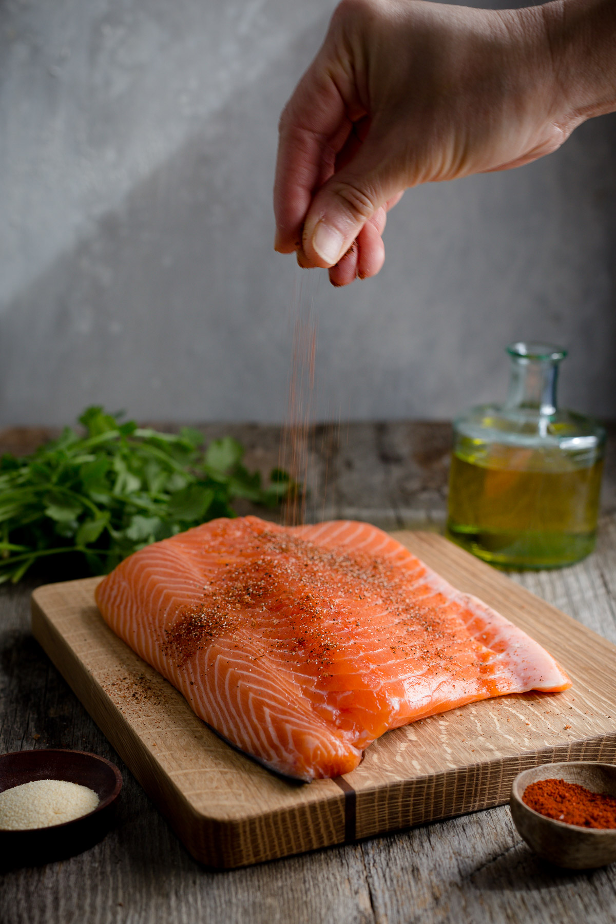 Spices being sprinkled on a side of salmon.