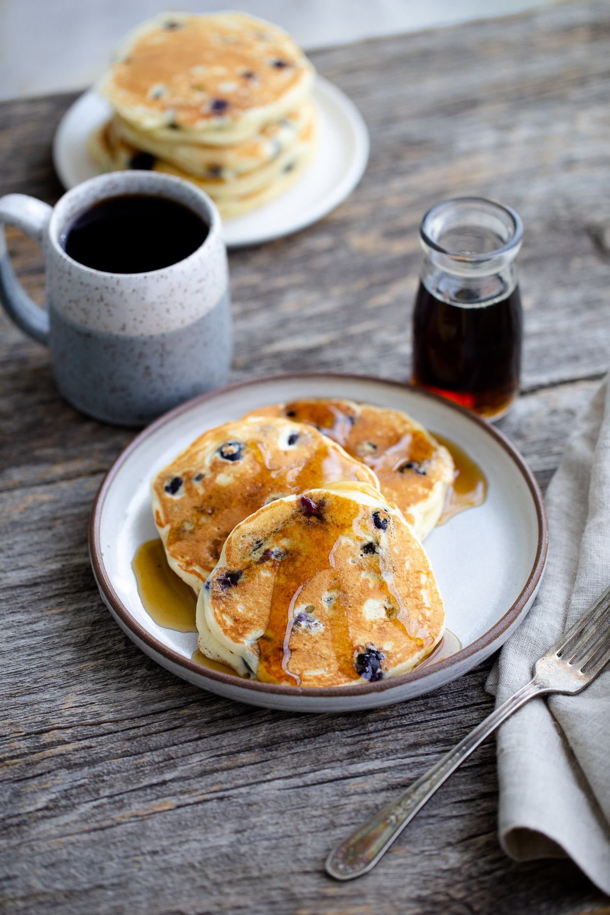 Pancakes drizzled with syrup on a plate next to a cup of coffee.