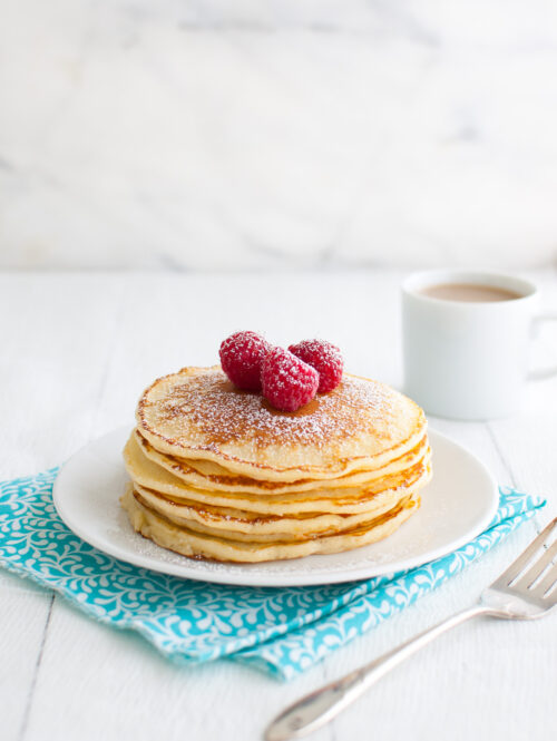 A stack of lemon soufflé pancakes garnished with powdered sugar and fresh raspberries on a white plate.