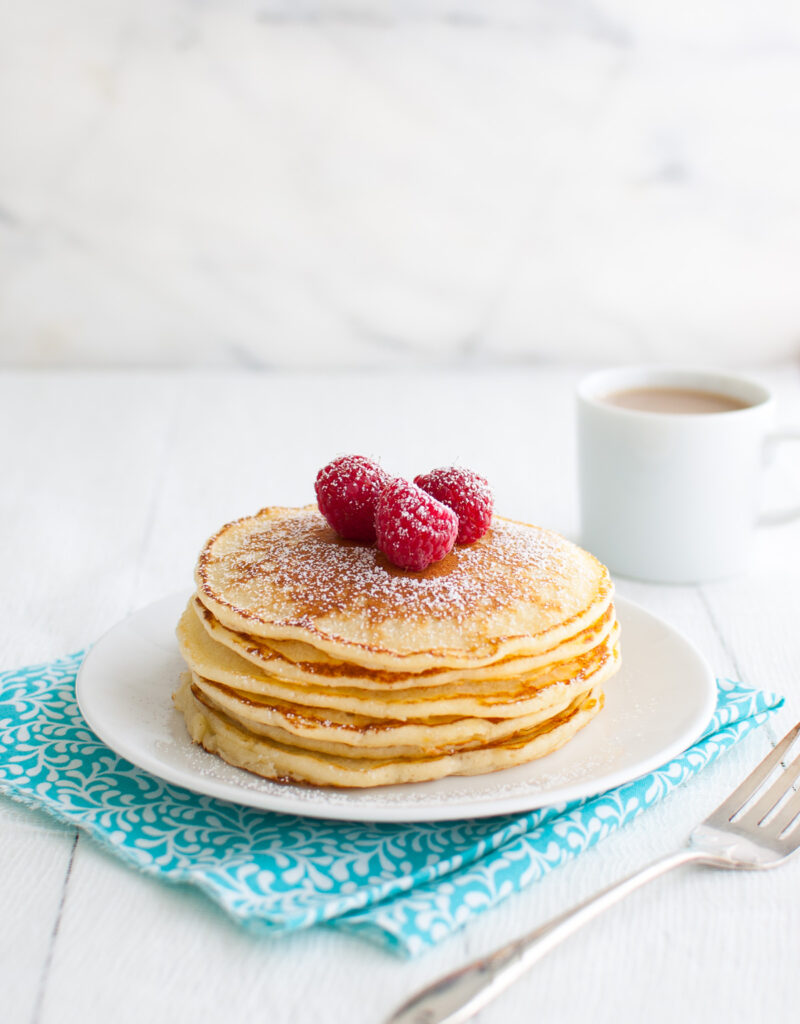 A stack of lemon soufflé pancakes garnished with powdered sugar and fresh raspberries on a white plate.