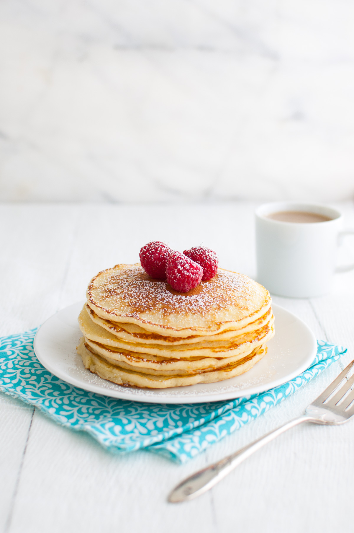 A stack of lemon soufflé pancakes garnished with powdered sugar and fresh raspberries on a white plate.