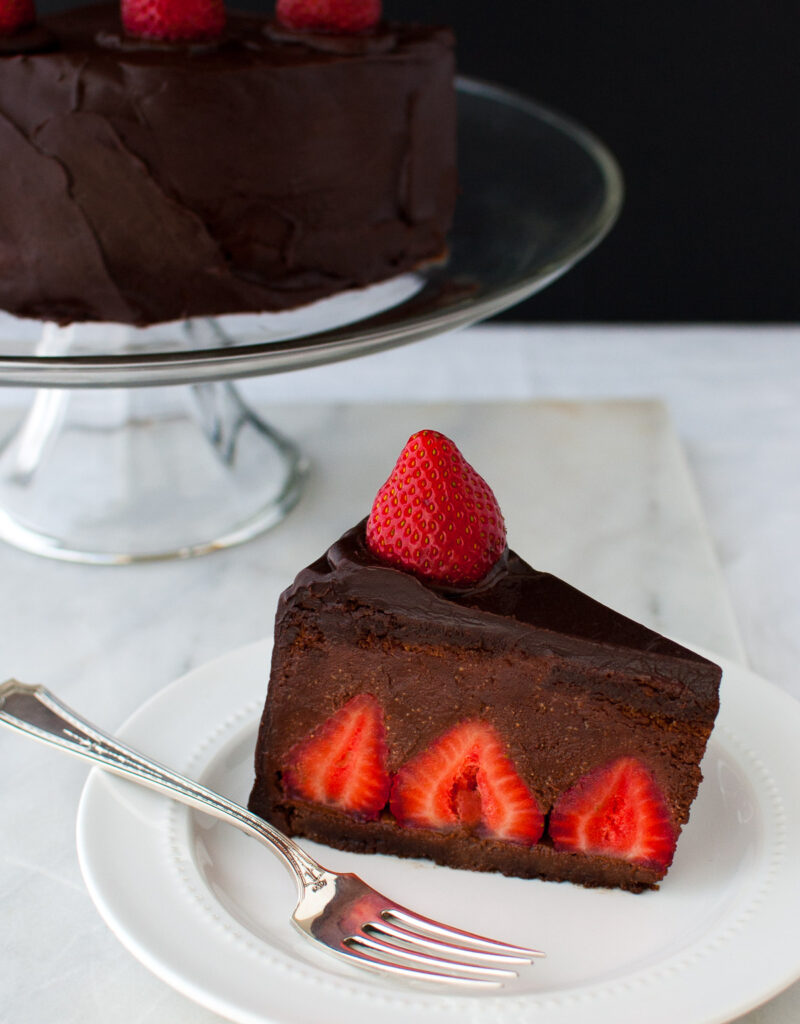 A slice of chocolate strawberry mousse cake on a white plate in front of a cake stand.