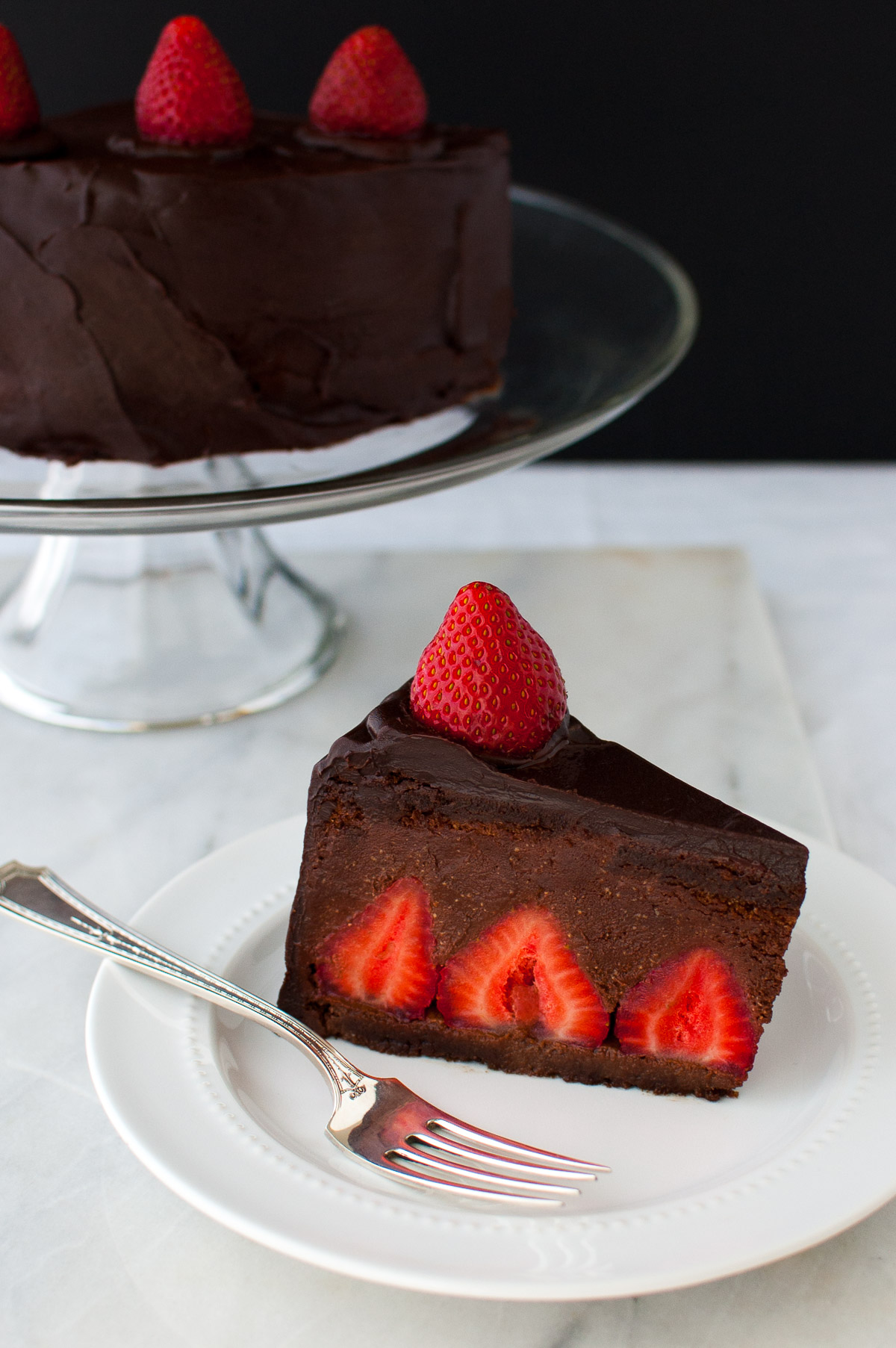 A slice of chocolate strawberry mousse cake on a white plate in front of a cake stand.