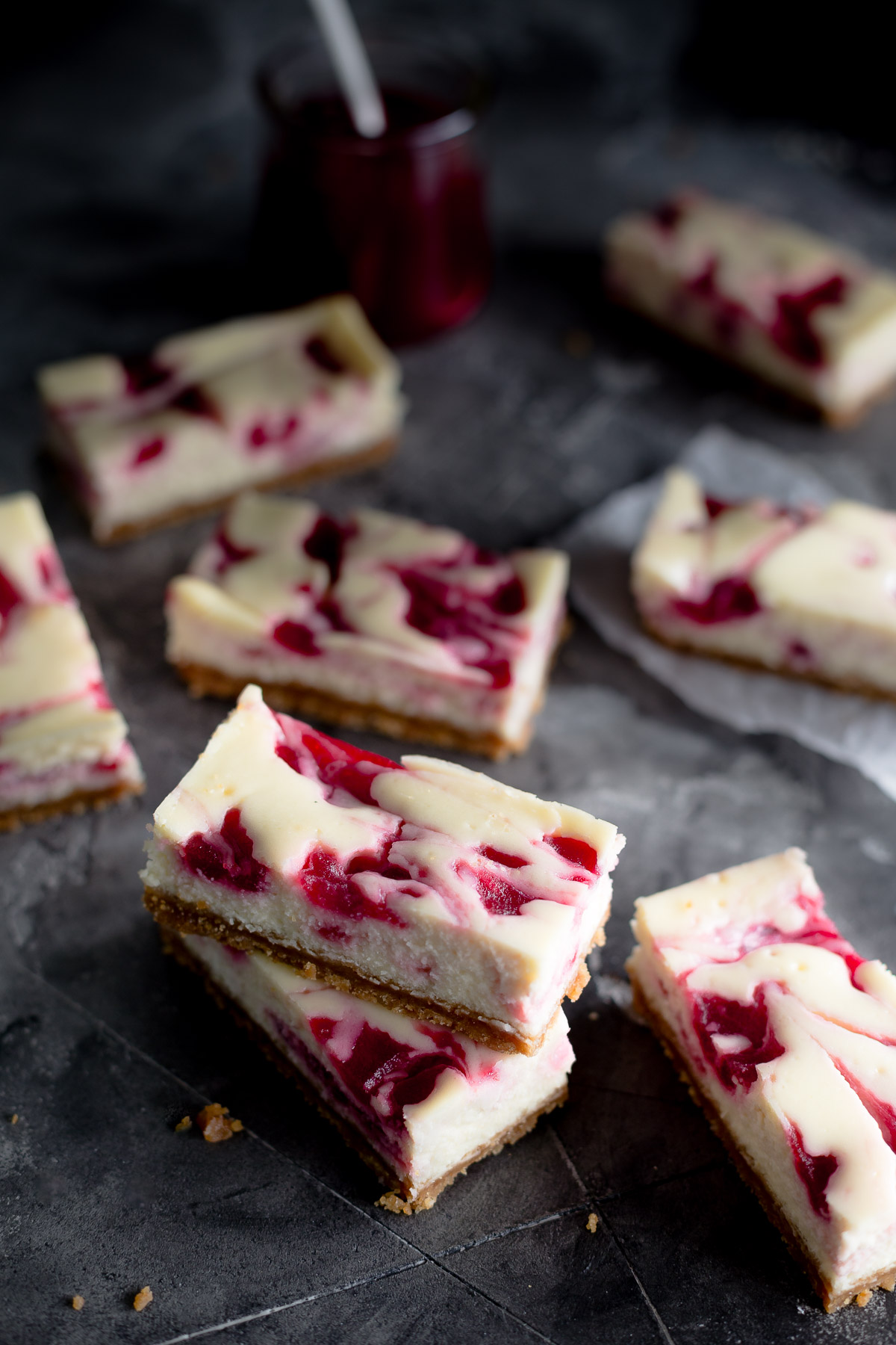 Some cranberry swirl cheesecake bars on a stone tabletop.