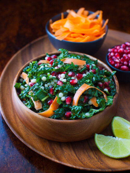 Pomegranate, Israeli couscous and kale salad in a wooden bowl.