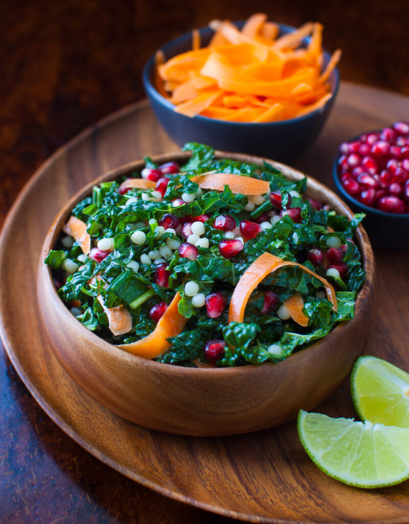 Pomegranate, Israeli couscous and kale salad in a wooden bowl.