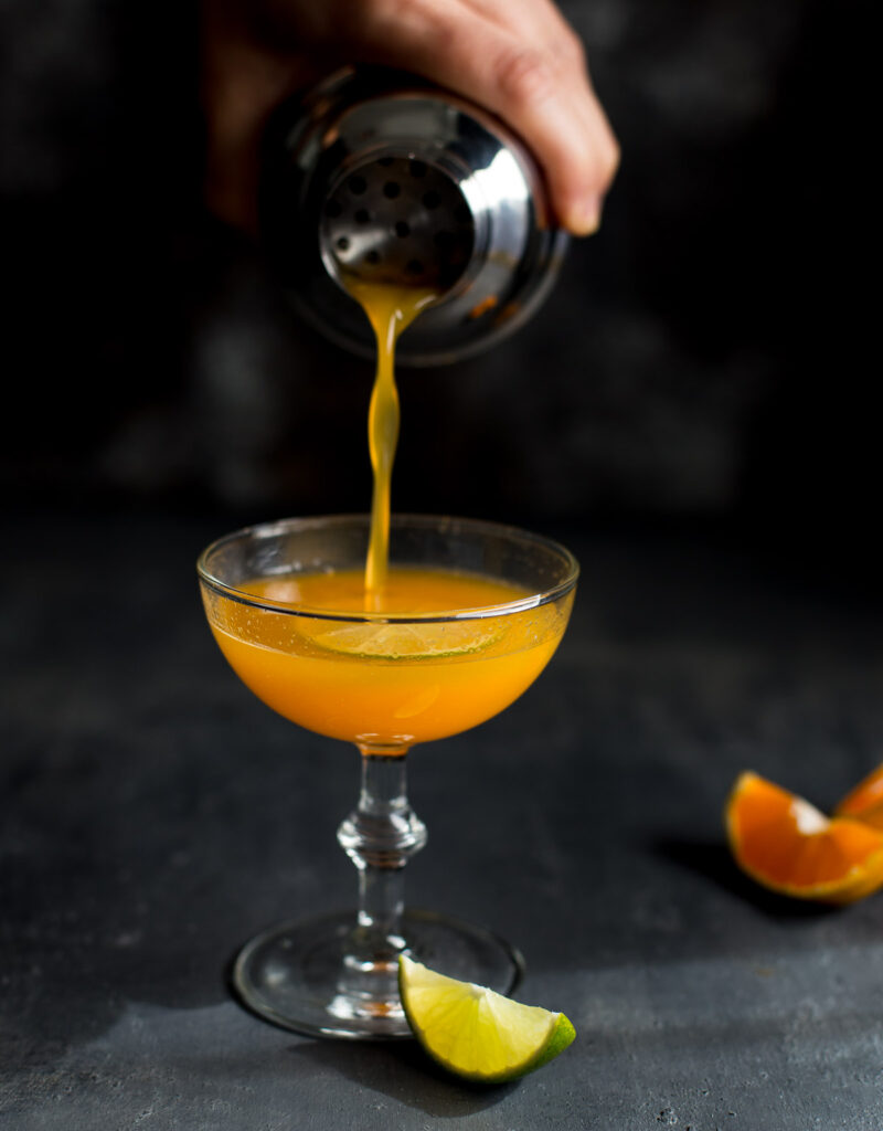 Orange vodka cocktail being poured from a shaker into a coupe glass.