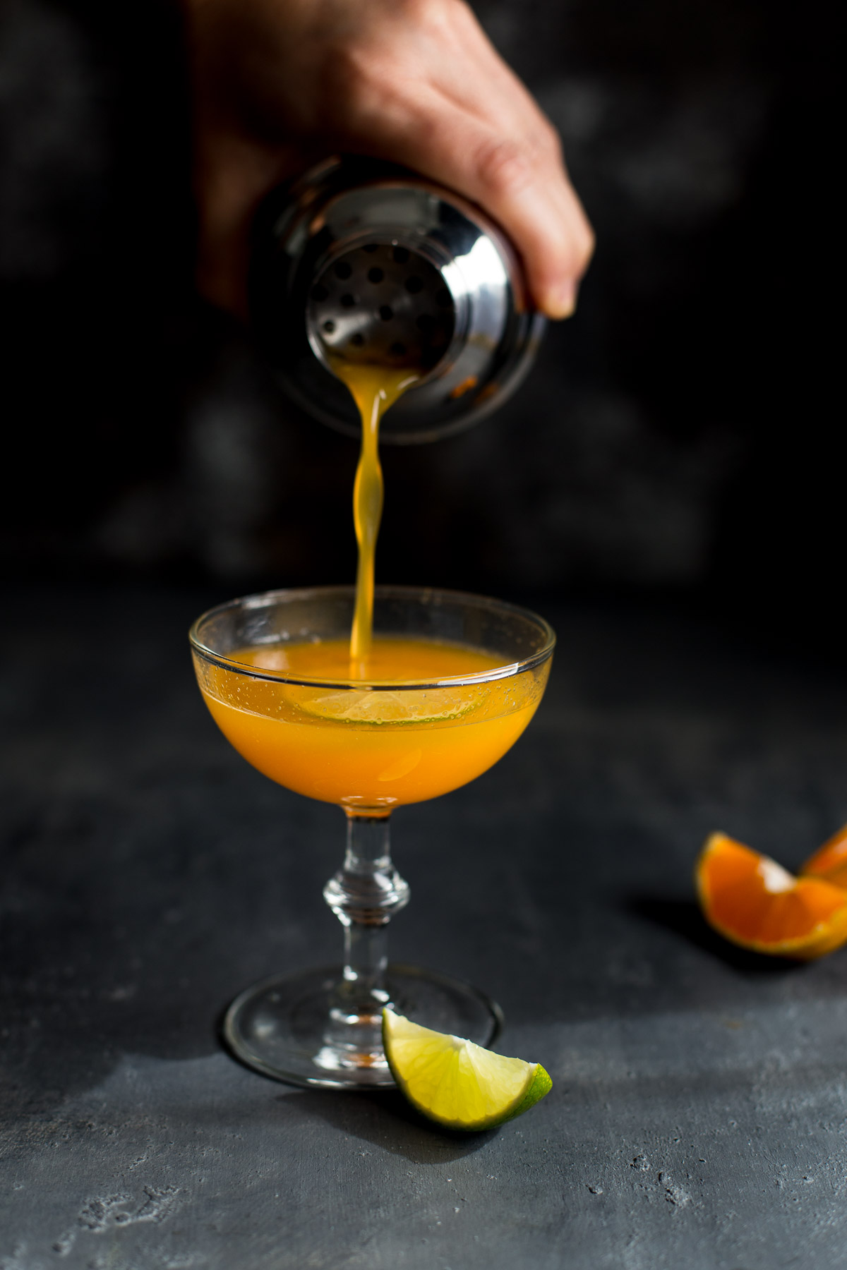 Orange vodka cocktail being poured from a shaker into a coupe glass.