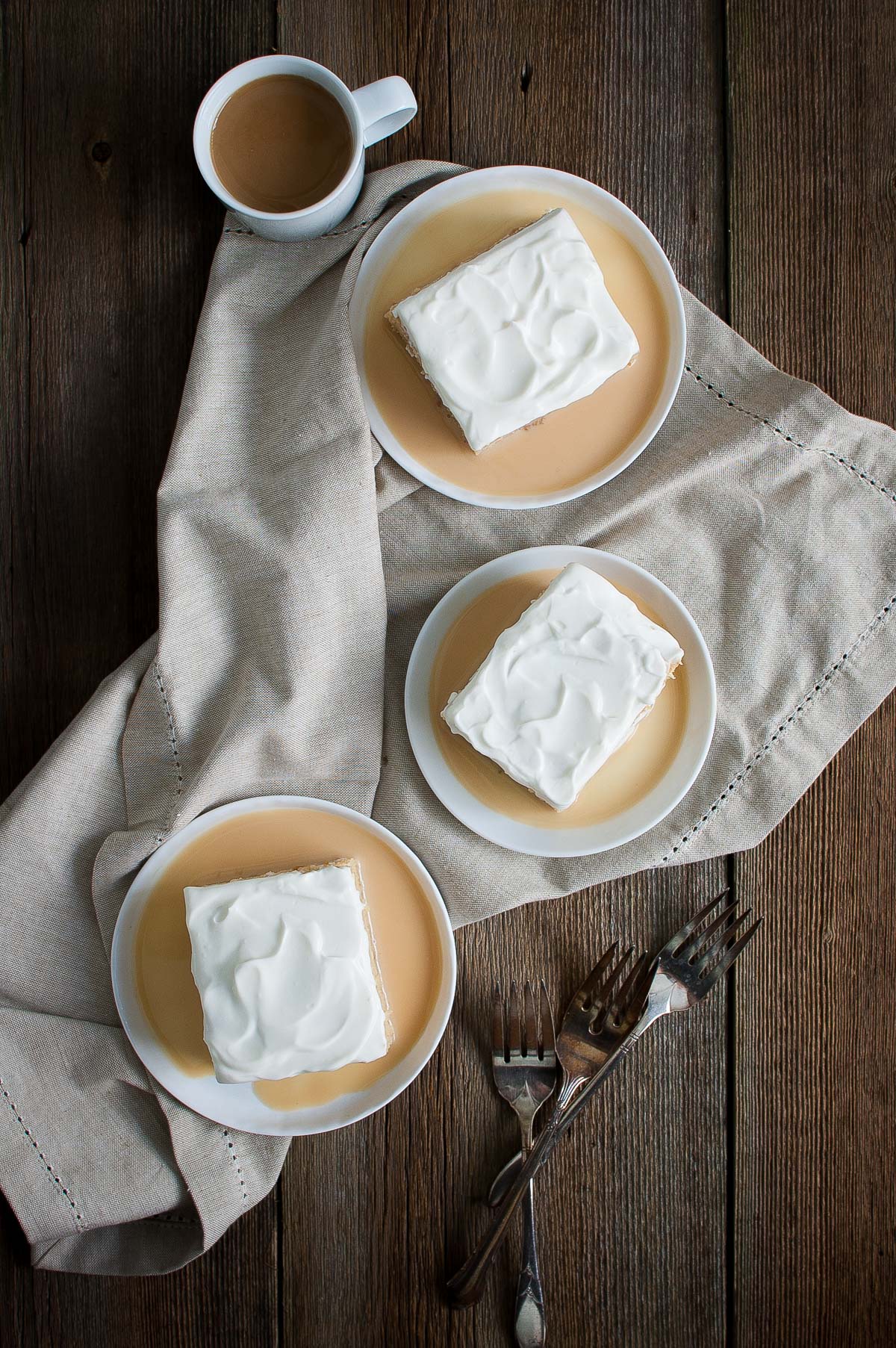 Three slices of tres leches cake on small white plates.