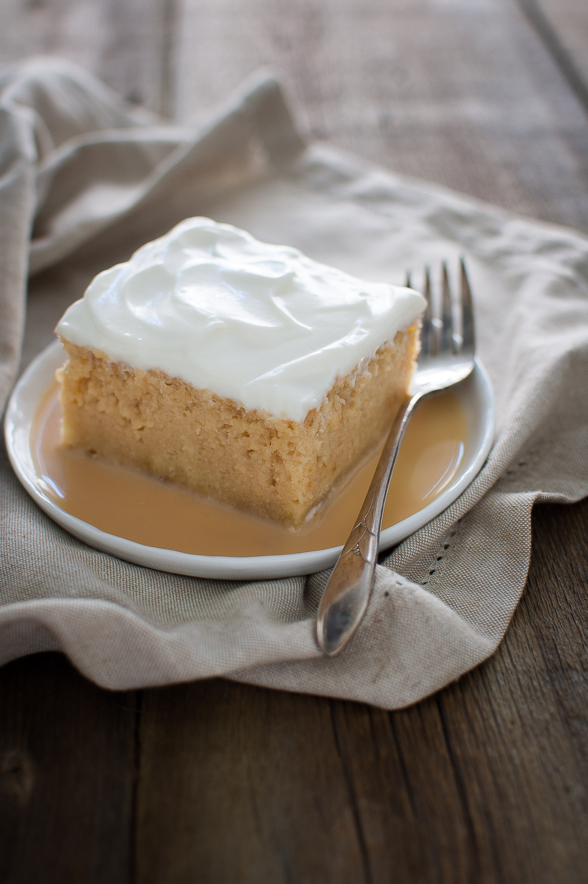 A slice of tres leches cake on a white plate.