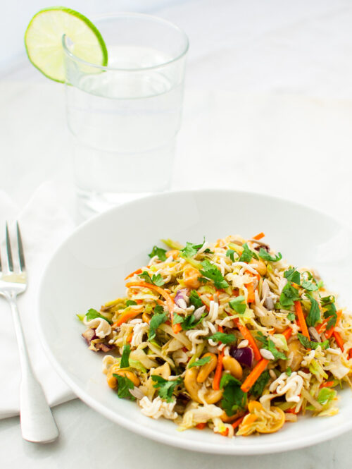 A bowl of salad next to a fork and a glass of water.