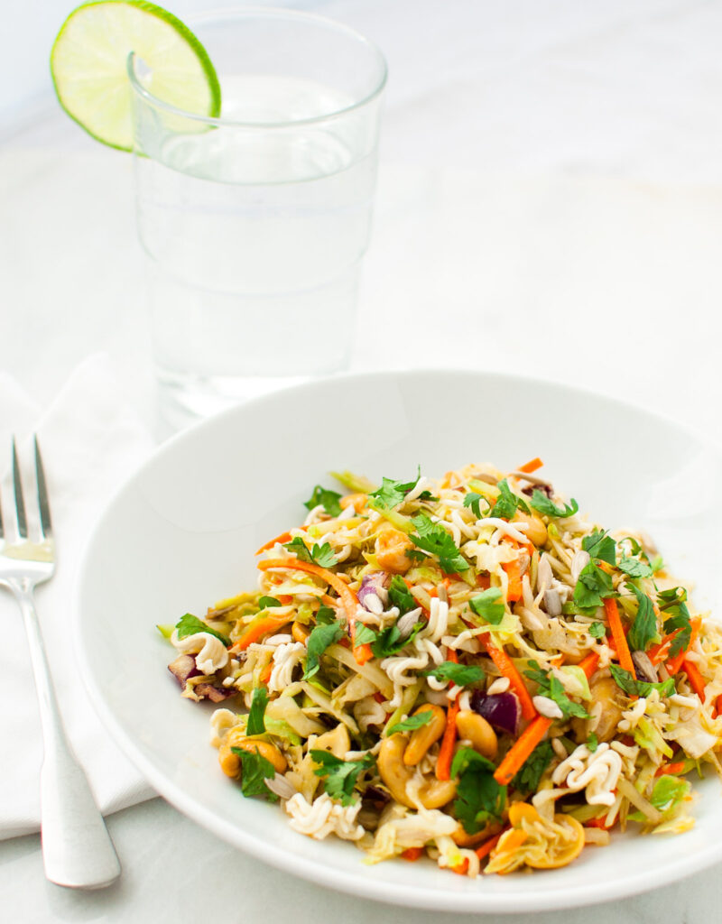 A bowl of salad next to a fork and a glass of water.