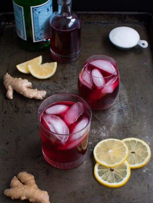 Two glasses of hibiscus ginger tea spritzer on a metal tray.
