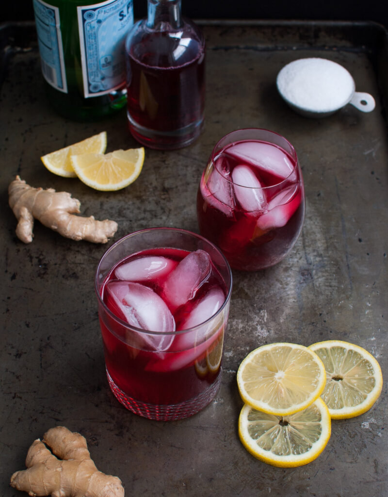 Two glasses of hibiscus ginger tea spritzer on a metal tray.