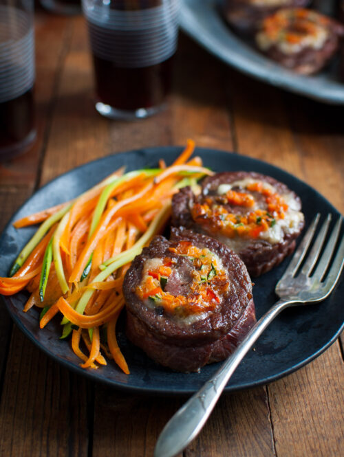 Stuffed steak rolls and some sautéed vegetables on a black plate.