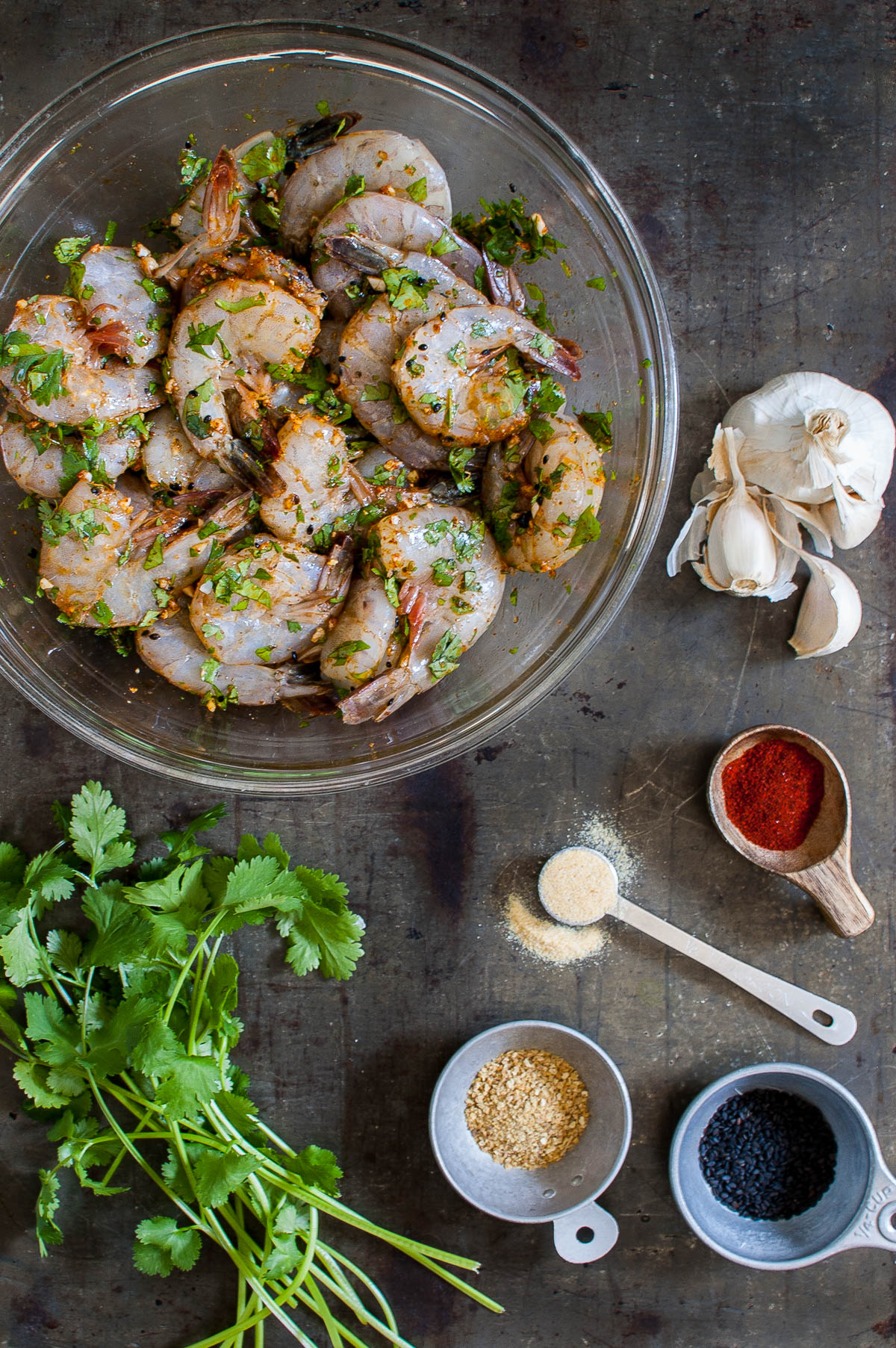 Marinated shrimp in a bowl next to some garlic, spices, and cilantro.