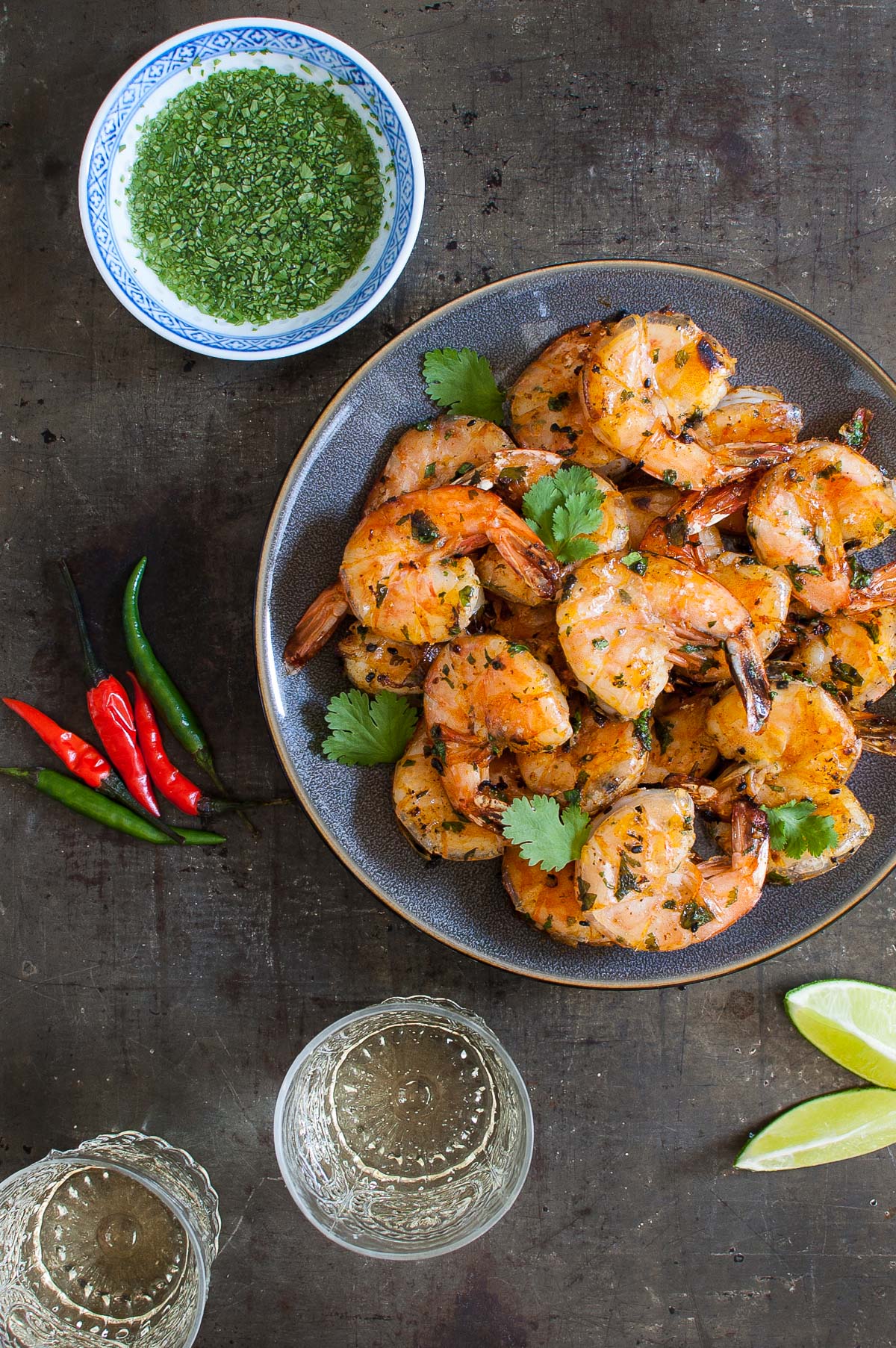 Thai grilled shrimp on a gray plate next to glasses of wine and extra sauce in a sauce dish.
