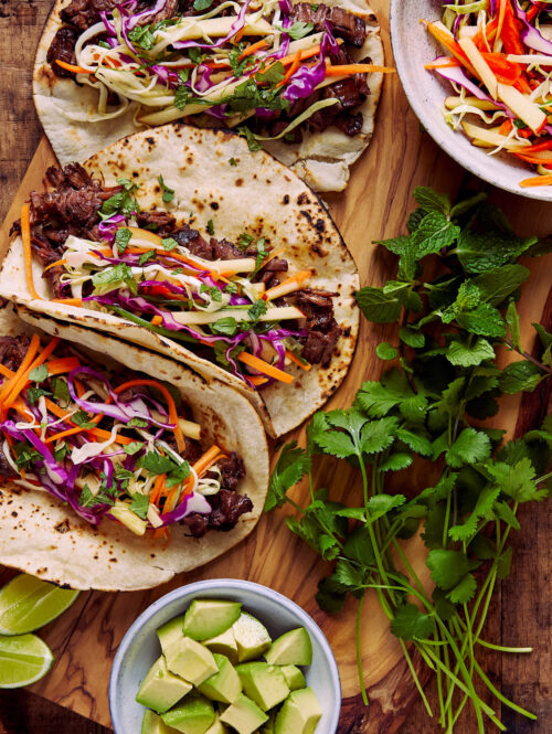 Beef tacos next to avocados, cabbage slaw, and cilantro.