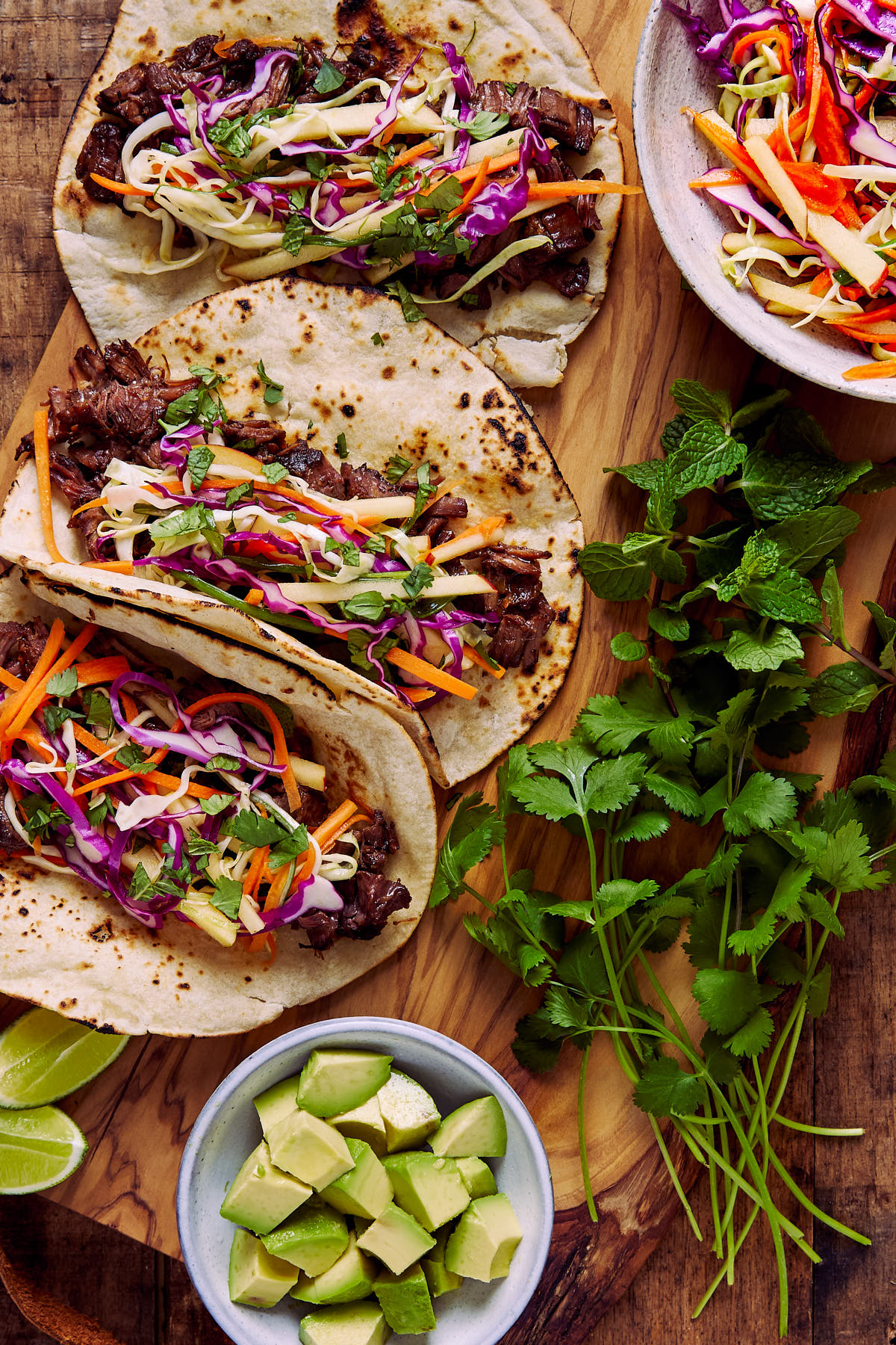 Beef tacos next to avocados, cabbage slaw, and cilantro.