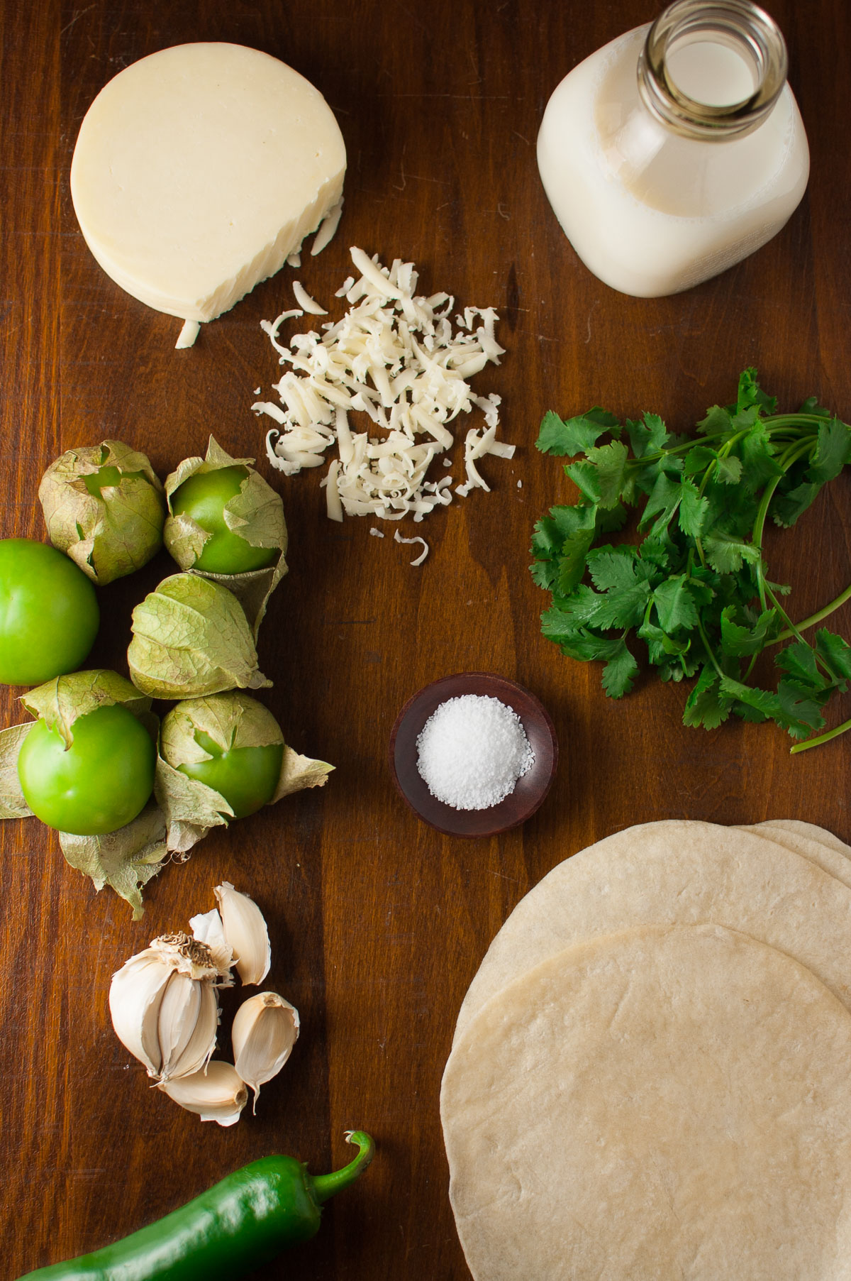 Ingredients for making chicken enchiladas and tomatillo sauce spread out on a wooden table top.