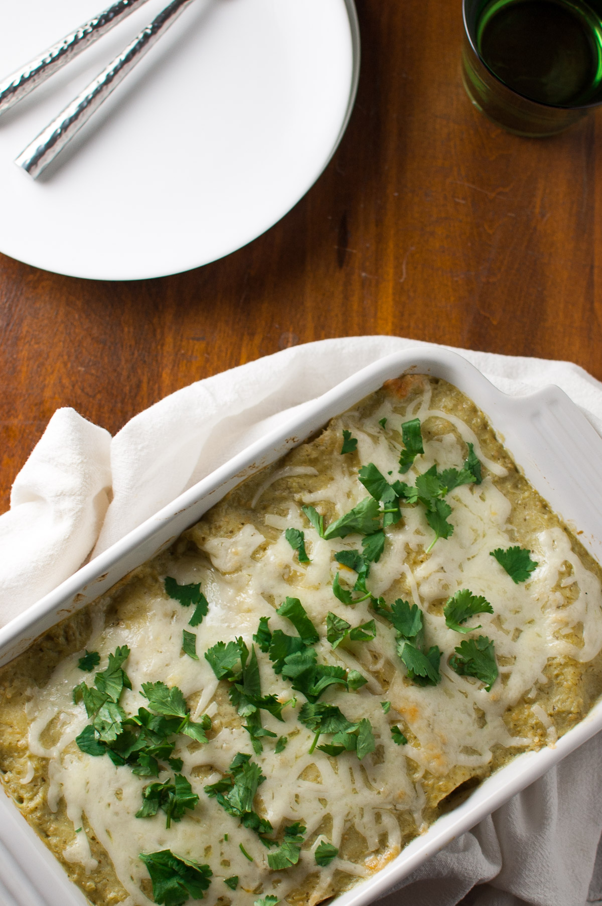 Chicken enchiladas topped with tomatillo sauce, melted cheese, and chopped cilantro in a white casserole pan.