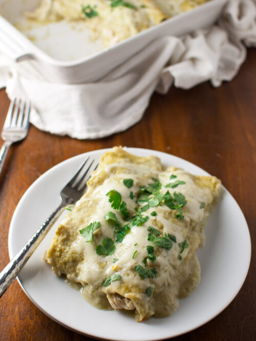 Chicken enchiladas topped with tomatillo sauce and melted cheese on a white plate.