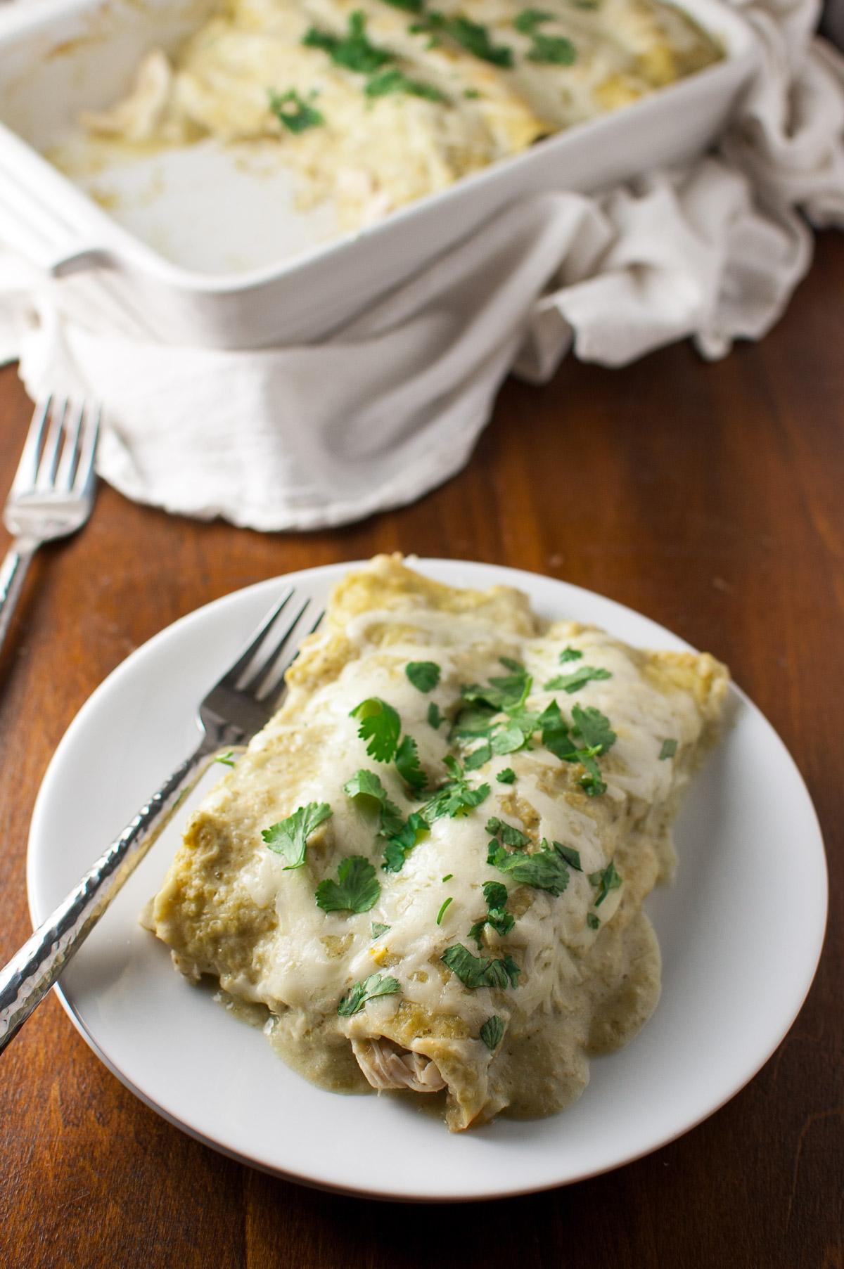 Chicken enchiladas topped with tomatillo sauce and melted cheese on a white plate.