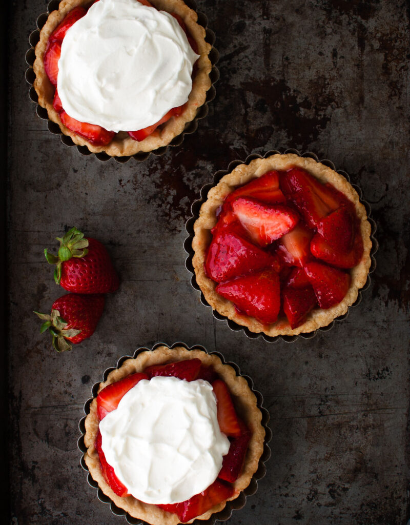 Three mini fresh strawberry pies on a metal surface.