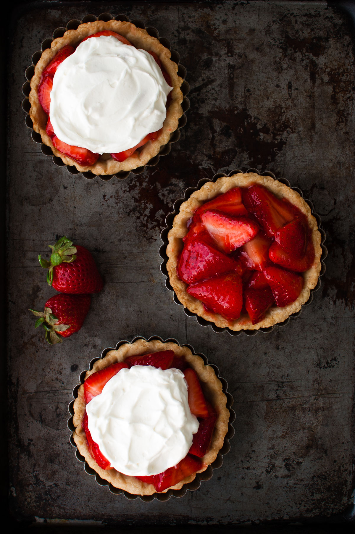 Three mini fresh strawberry pies on a metal surface.
