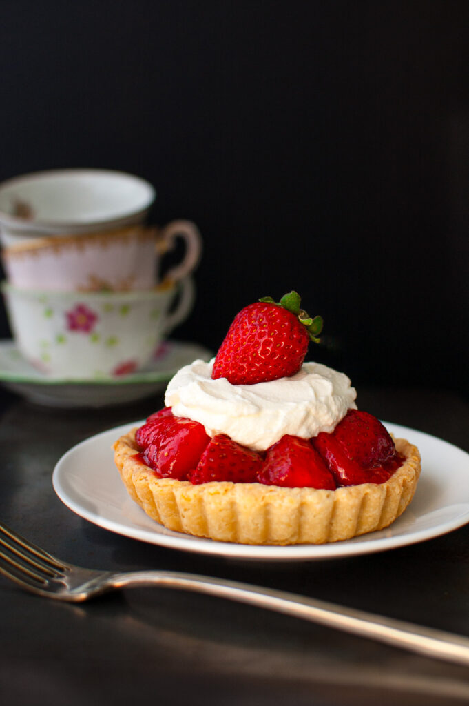 A mini fresh strawberry pie topped with whipped cream on a white plate.