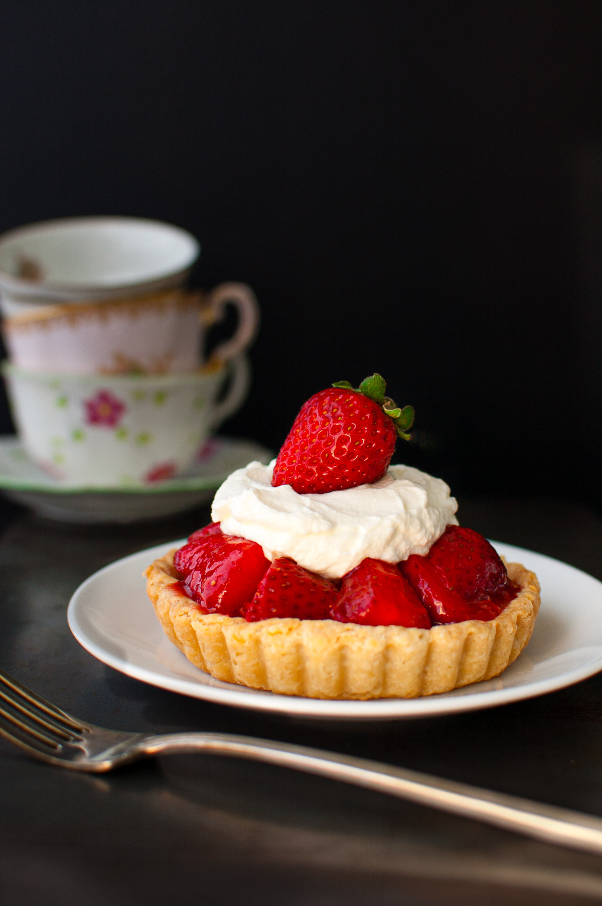 A mini fresh strawberry pie topped with whipped cream on a white plate.
