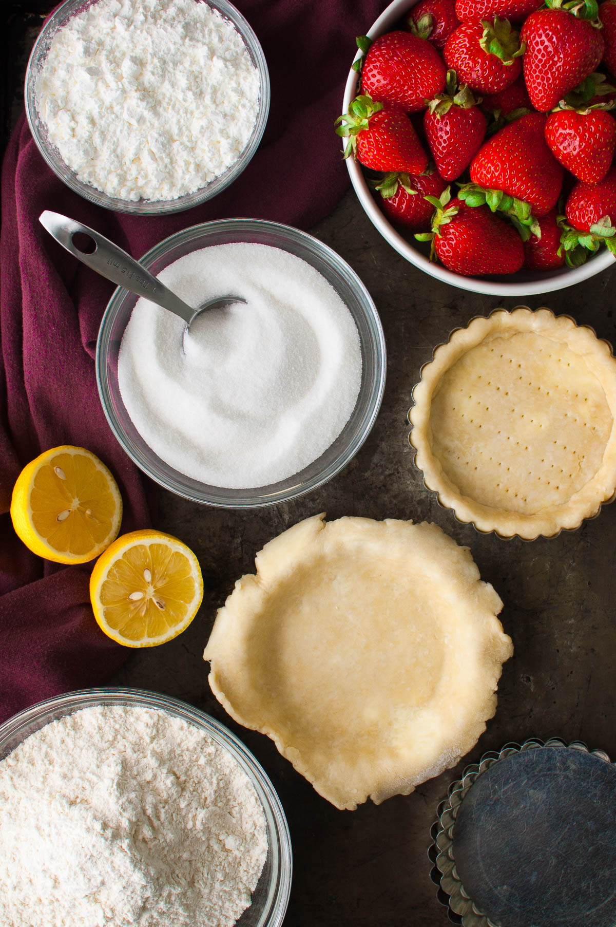 Ingredients for making fresh strawberry pies set out on a metal tray.