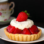 A mini fresh strawberry pie topped with whipped cream on a white plate.