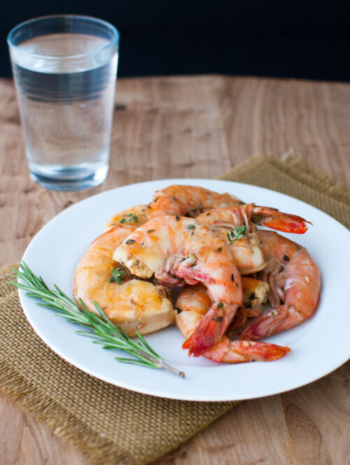 Lemon and herb grilled shrimp on a white plate garnished with a sprig of rosemary.