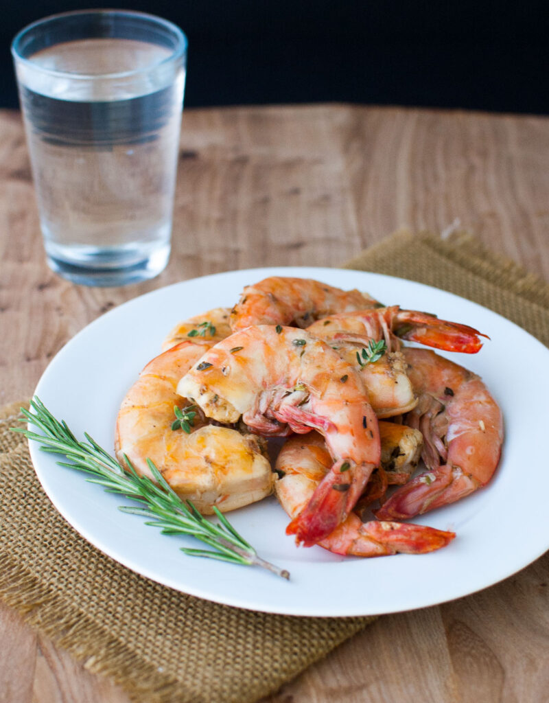 Lemon and herb grilled shrimp on a white plate garnished with a sprig of rosemary.