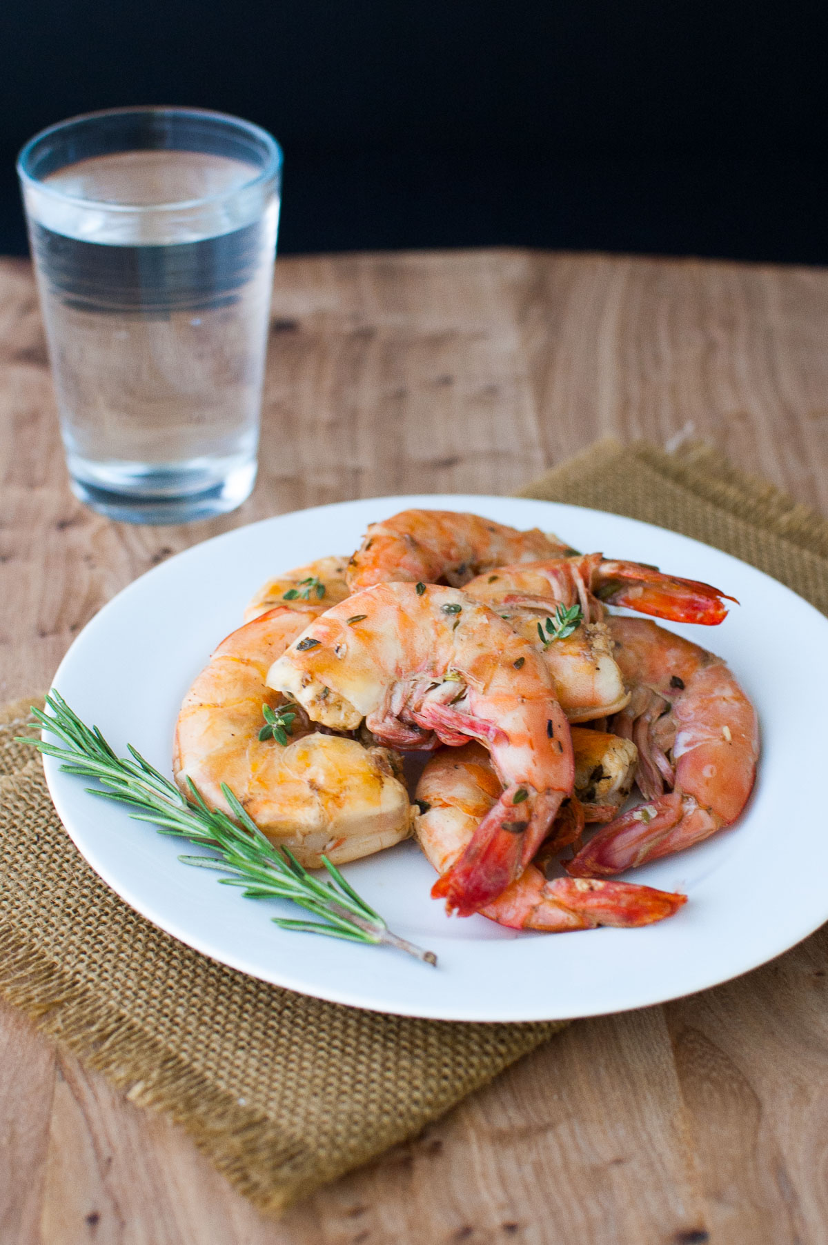 Lemon and herb grilled shrimp on a white plate garnished with a sprig of rosemary.