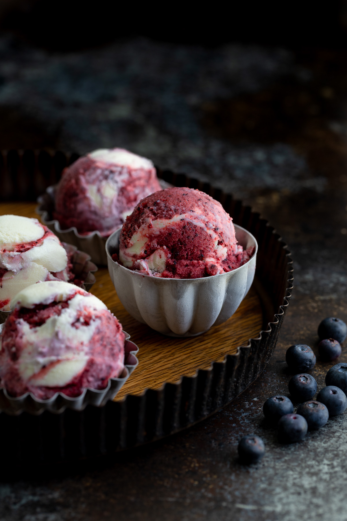Scoops of blueberry sorbet vanilla swirl ice-cream in metal bowls on a serving tray.