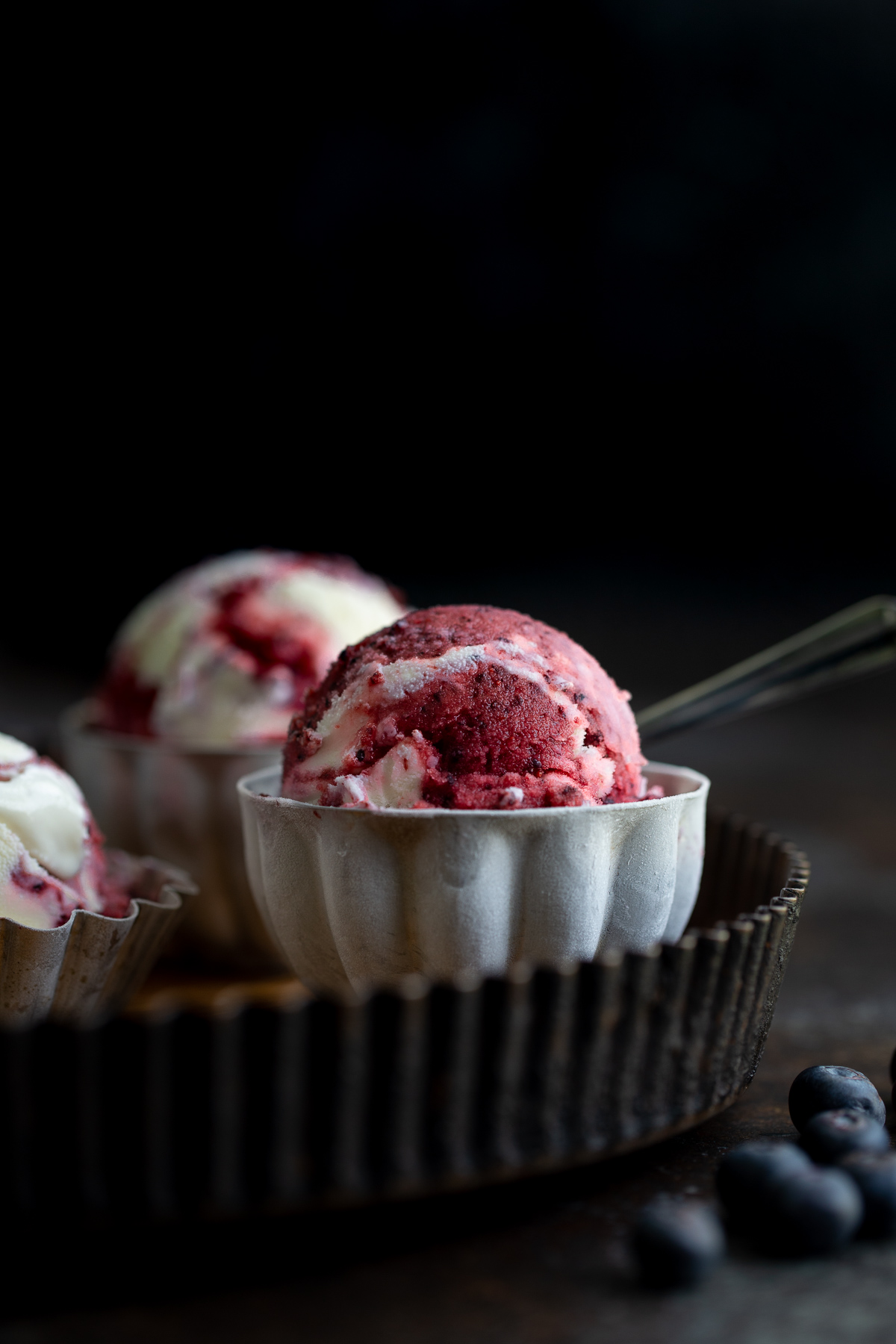 Close-up photo of a scoop of blueberry sorbet vanilla swirl ice-cream in a metal bowl.
